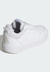 Zapatilla deportiva blanca con materiales de malla y sintéticos, con perfil bajo, puntera redonda, detalles texturizados y tres rayas diagonales.