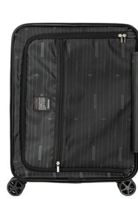 La valigia nera a ruote presenta un interno in tessuto testurizzato con un sottile motivo a righe, molteplici scomparti con zip e tasche organizzative.