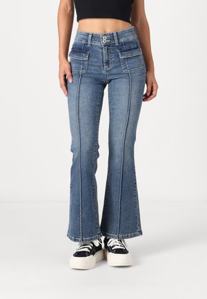 Kvinde iført blå cowboybukser med høj talje og vide ben med forlommer og sort-hvide platform sneakers.