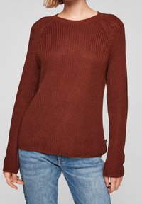 Gebreide trui in diep roestkleur, uitgevoerd met een ronde hals, lange mouwen, gestructureerde stof en geribbelde boorden, gecombineerd met lichtblauwe spijkerbroek.