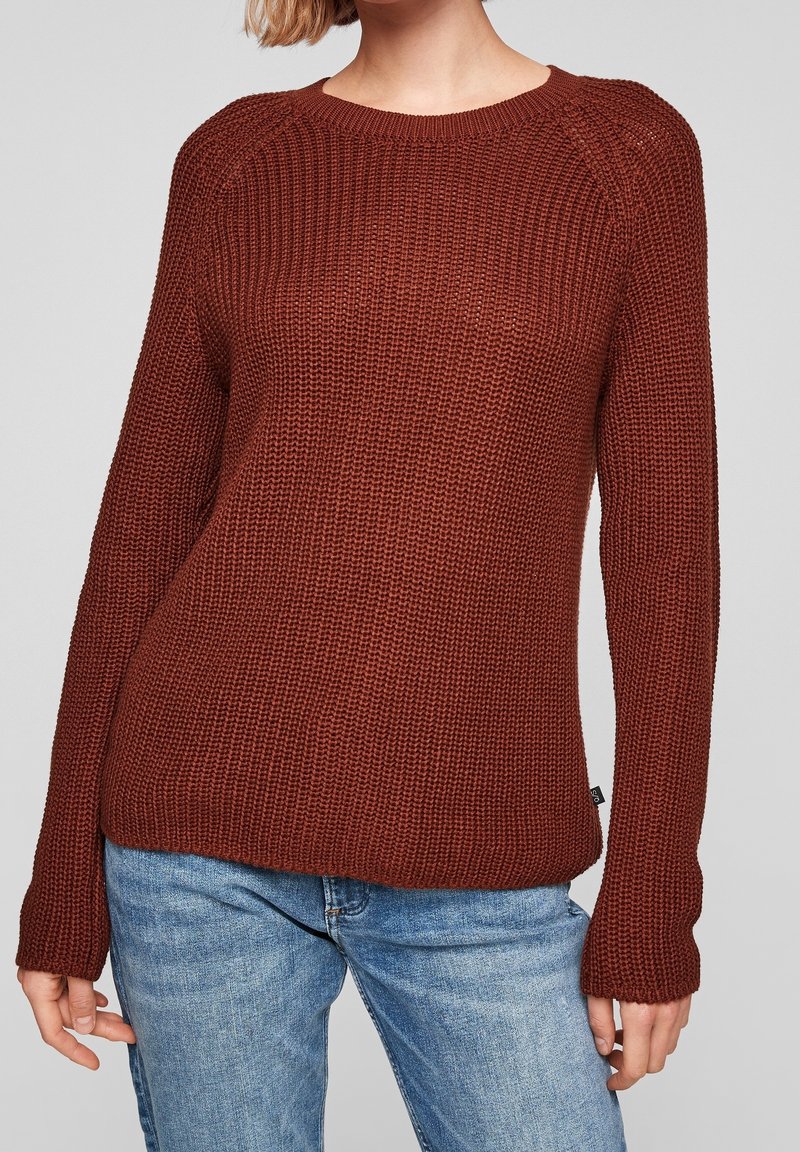 Gebreide trui in diep roestkleur, uitgevoerd met een ronde hals, lange mouwen, gestructureerde stof en geribbelde boorden, gecombineerd met lichtblauwe spijkerbroek.