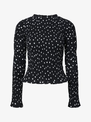 Svart teksturert bluse med hvite polkadotter; har lange ermer, en volangkant og rynkede detaljer rundt overdelen og ermene.