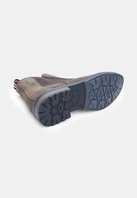 Bota de ante marrón con paneles de malla texturizados, suela de goma con un patrón de dibujo en diamante y detalle en el talón a rayas contrastantes.