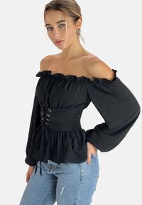 Sort off-the-shoulder top med gathered ærmer, et smocket talje med snøre detaljer og en let, svajende kant. Kombineret med lyseblå jeans.