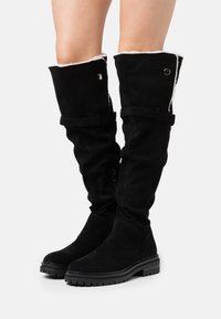 Czarne kozaki za kolano zamszowe z miękką wyściółką. Charakteryzują się niską gumową podeszwą, regulowanymi paskami oraz srebrnymi ozdobami.