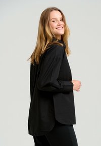 Sort langærmet skjorte med knapkrave, skræddersyet pasform og buet underkant. Stoffet ser glat og let ud.