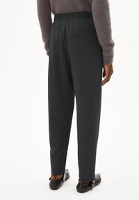 Donkere grijze joggers met een elastische tailleband, taps toelopende benen en een klein achterzakje. Glad stof met een zachte textuur.