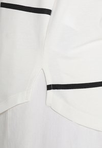 Vit t-shirt med svarta horisontella ränder, med en rundad fåll och sidoflik för extra detaljer. Tillverkad av mjukt bomullsmaterial.