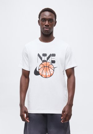 Mees kannab valget t-särki musta Nike tekstiga ja Swooshi logoga, mille keskel on oranž korvpalligraafika, seisab valgel taustal.