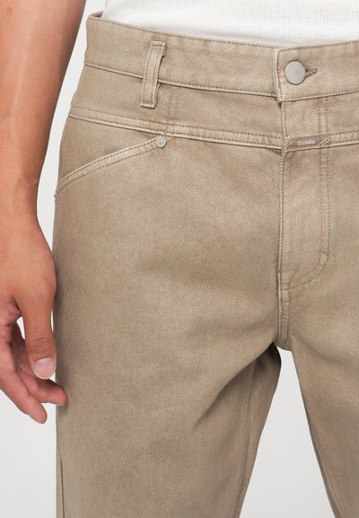 Beige színű, slim fit farmernadrág, öt zsebbel, fém kiegészítőkkel és diszkrét varrási részletekkel az illeszkedéseknél.