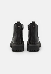 Botines de cuero negro con suela de goma gruesa. Cuentan con una lengüeta, paneles laterales elásticos y texto grabado en los tacones traseros.