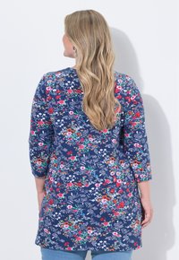 Blumen-Tunika aus dunkelblauem Stoff mit 3/4-Ärmeln. Sie verfügt über einen lebhaften Blumenprint in Rot, Pink und Weiß. Gerade Säume mit lockerer Passform.