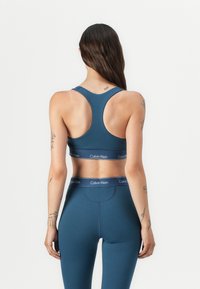 Temno modra športna modrc s športnim hrbtom; ima pas z logotipom Calvin Klein. Stiliziran z ujemajočimi se visokim pasom hlačami.