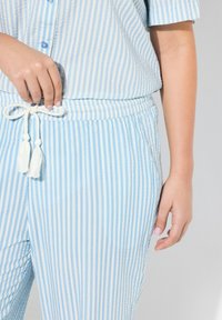 Camicia a righe azzurro chiaro e pantaloni abbinati con vita elastica, dotati di una cravatta con frange. Texture stropicciata, maniche corte.