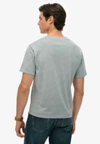 Grå t-shirt med korte ærmer i glat stof. Har rund halsudskæring og minimale syningsdetaljer. Bæres med mørkeblå jeans.