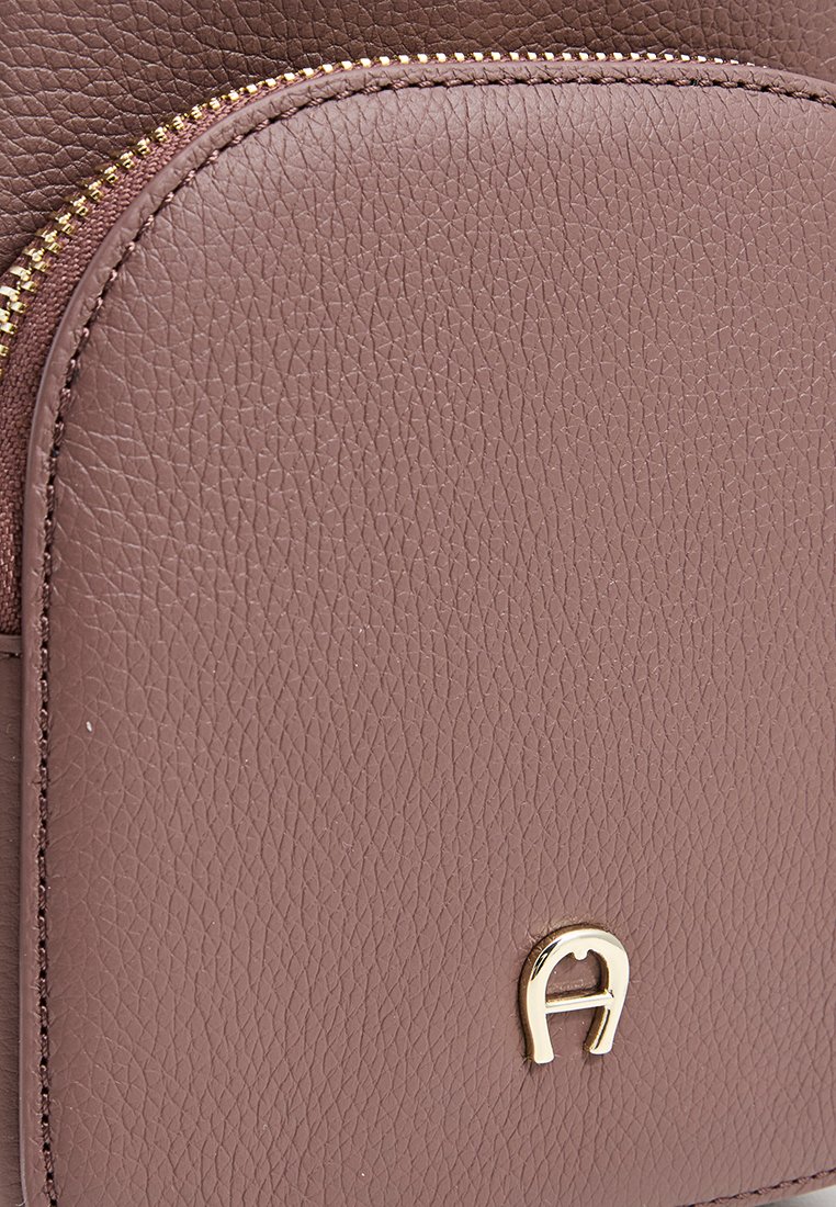 Nahaufnahme einer braunen, strukturierten Lederhandtasche mit goldfarbenem Reißverschluss und kleinem goldfarbenem Metallemblem auf der Vorderseite.