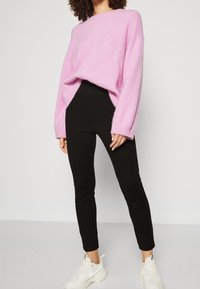Pink oversized knit sweater with wide sleeves paired with black fitted leggings and white sneakers. Smooth texture, relaxed fit.