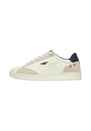 Sneaker basse bianche e beige con lacci bianchi, linguetta nera sul tallone, testo in rilievo "Aeronautica Militare" e piccolo dettaglio della bandiera italiana sul lato.