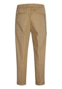 Pantalons en coton beige avec une taille élastique, deux poches arrière et un détail de chaîne sur le côté. Design à jambes fuselées avec des chevilles côtelées.