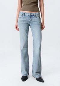 Svetlo modre razširjene kavbojke iz jeansa z nežnim bledenjem, z obliko s petimi žepi in kontrastnim šivanjem. Dopasirane s topom olivno zelene barve.