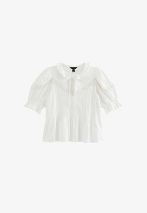 Blusa blanca de manga corta con cuello fruncido, detalle de encaje en el pecho y las mangas, escote con abertura en forma de ojo de cerradura con lazo, y bajo estilo peplum.