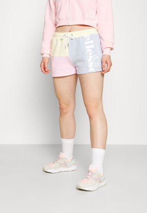 Osoba nosząca pastelowe szorty z białym sznurkiem, białe skarpetki, różowo-beżowe trampki oraz krótki różowy sweatshirt.