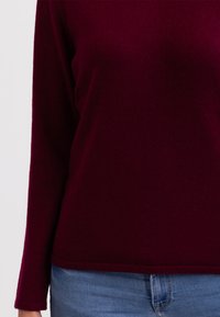 Jersey de manga larga burdeos en suave tejido de punto, con cuello redondo y un dobladillo recto, combinado con unos vaqueros de mezclilla azul claro.