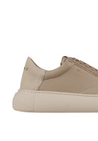 Sneaker in pelle beige con pannelli texturizzati, punta rotonda e suola in gomma spessa. Presenta dettagli dorati e lacci decorati.