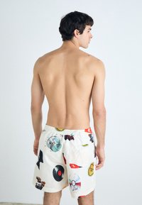 Herreshorts til svømming i hvit tekstil med fargerike grafiske trykk av musikalske elementer. Har elastisk midjebånd og en baklomme.