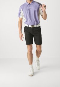 Polo shirt court à manches courtes violet et gris, avec un col, associé à des shorts noirs. Une ceinture blanche accentue la tenue. Des chaussures de golf blanches complètent le look.