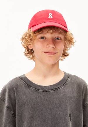 Rode katoenen pet met een verstelbare band, voorzien van een klein wit logo aan de voorkant. De persoon draagt een vervaagde grijze sweatshirt.