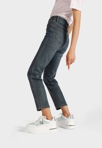 Jeans in denim blu scuro con una vestibilità slim e lunghezza cropped, abbinati a sneaker con platform bianche con dettagli verde menta e particolari argentati.