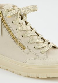 Beige High-Top-Sneaker mit strukturierten Schnürsenkeln, die zu einer Schleife gebunden sind, einem seitlichen goldenen Reißverschluss und einer dicken, geriffelten Sohle.