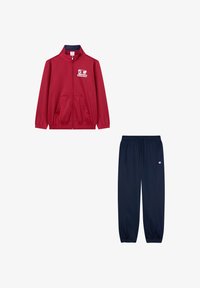 Chaqueta roja con cremallera y bolsillos laterales, con el logo de Champion, combinada con pantalones de chándal azul marino que tienen cordón y un acento de logo.