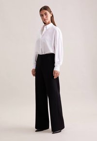 Witte oversized blouse met opbollende mouwen, gecombineerd met zwarte broek met brede pijpen. Glad stof, eenvoudig ontwerp en een aansluitend silhouet.