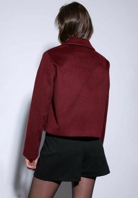 Bordeauxcropped jack met een kraag, gemaakt van een zachte stof; beschikt over lange mouwen en een strak, minimalistisch ontwerp.
