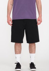 Shorts en denim noir à coupe droite, longueur genou. Associés à un t-shirt violet, des chaussettes de sport blanches et des baskets noires.