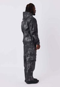 Schwarze Batikjacke mit Kapuze, einfarbigen Bündchen und passender Cargo-Hose mit mehreren Seitentaschen und lässigem Schnitt. Sehr glatte Textur.