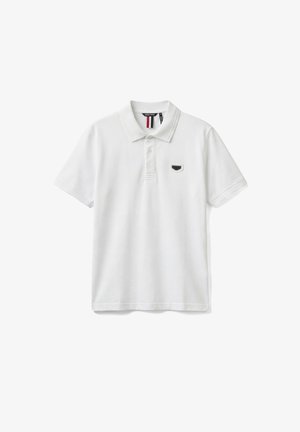 Polo bianca a maniche corte con colletto a coste, patta con due bottoni ed emblemma piccolo a scudo nero e grigio sul petto a sinistra.