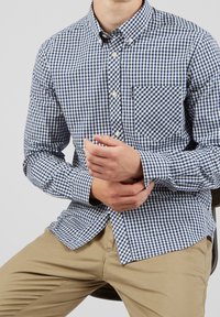 Blue and white checkered button-up shirt with a chest pocket, featuring a classic collar and long sleeves, paired with khaki pants.