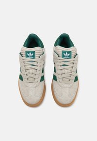 Baskets Adidas avec une tige en suede gris, des accents verts et une semelle en caoutchouc texturé. Le design comprend les trois bandes classiques.