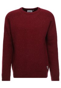 Punainen neulepaita, jossa on pyöreä kaula-aukko, raglan-hihat ja pilkullinen pinta. Sisältää pienen merkkipatchin helmassa yksityiskohtana.