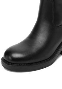 Must nahast pahkluu saabas ümmarguse varbaosaga, sileda tekstuuri, minimaalsete õmblustega ja paksu musta kummist tallaga. Ilma dekoratiivsete detailideta.