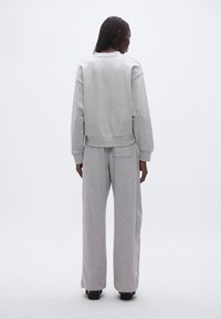 Harmaa collegepaita ja leveälahkeiset housut pehmeästä kankaasta. Neulotulla pääntiellä, resorimittoisilla hihoilla ja housuissa paikka tasku.