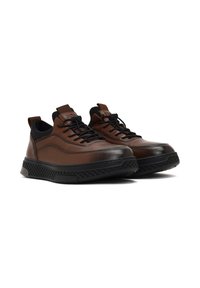 Des baskets en cuir marron présentent un design épuré, une semelle texturée noire avec un détail en mesh, et des lacets ronds. Étiquettes à l'arrière pour un enfilage facile.