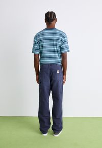 Striped teal and navy t-shirt paired with navy cargo pants featuring large pockets. The outfit has a relaxed fit and is complemented by white sneakers.