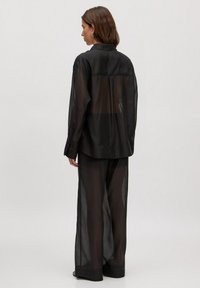Zwarte doorzichtige blouse met lange mouwen en bijpassende broek, met een losse pasvorm en een minimalistisch ontwerp, met een doorschijnende textuur.
