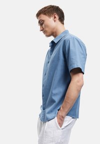 Lichtblauw overhemd met korte mouwen, gemaakt van een gestructureerde stof, met een knoopsluiting aan de voorkant en een standaard kraag, gecombineerd met witte broek.