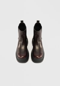 Κεραμιδί δερμάτινα μποτάκια μέχρι τον αστράγαλο με παχείς μαύρους καουτσούκ σόλες, διαθέτοντας λεία υφή και ελαστικές πλευρικές πάνελ για εύκολη χρήση.