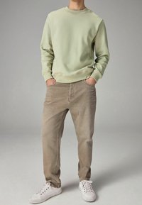 Felpa verde chiaro con collo a giro, abbinata a pantaloni beige. Sneakers bianche completano l'outfit, creando un look casual.